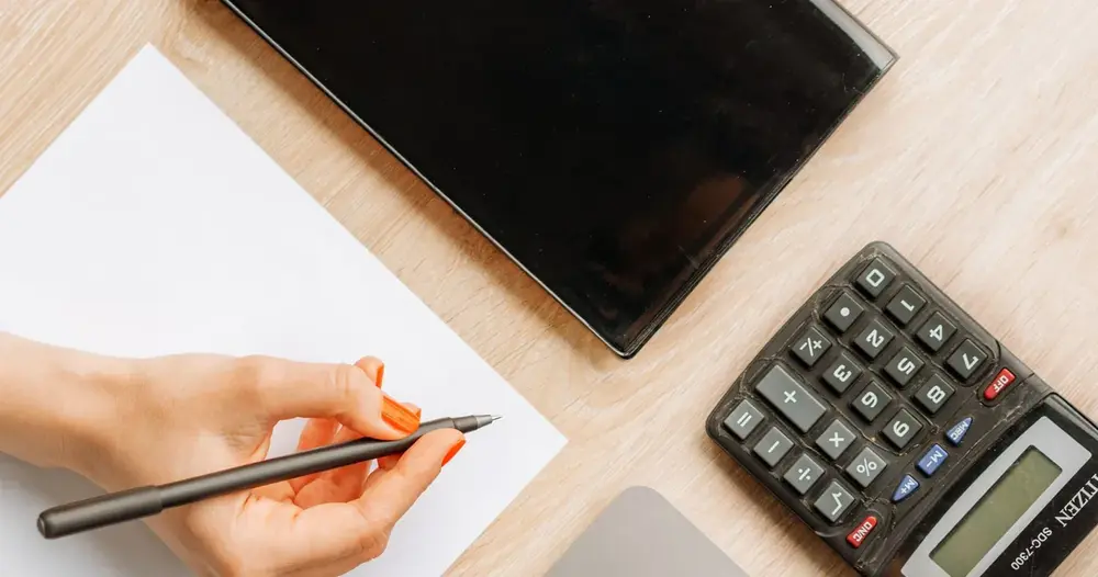 Mão escrevendo em papel ao lado de uma calculadora, imagem para gerar CNPJ válido para teste